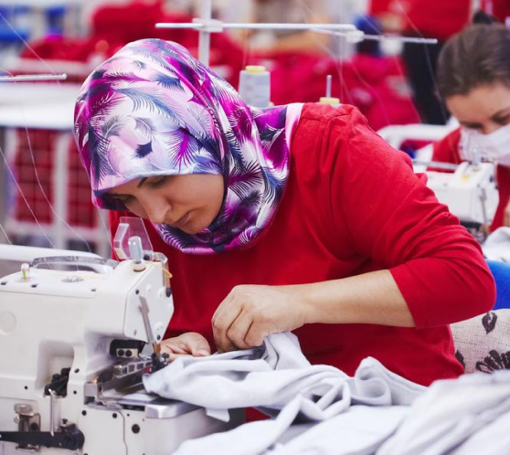 Woman in colourful headscarf using a sewing machine in factory