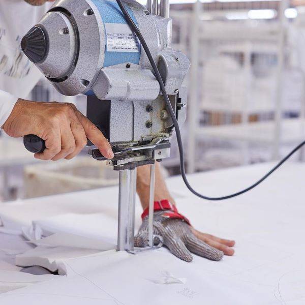 Man wearing protective glove cutting white fabric with cutting machine