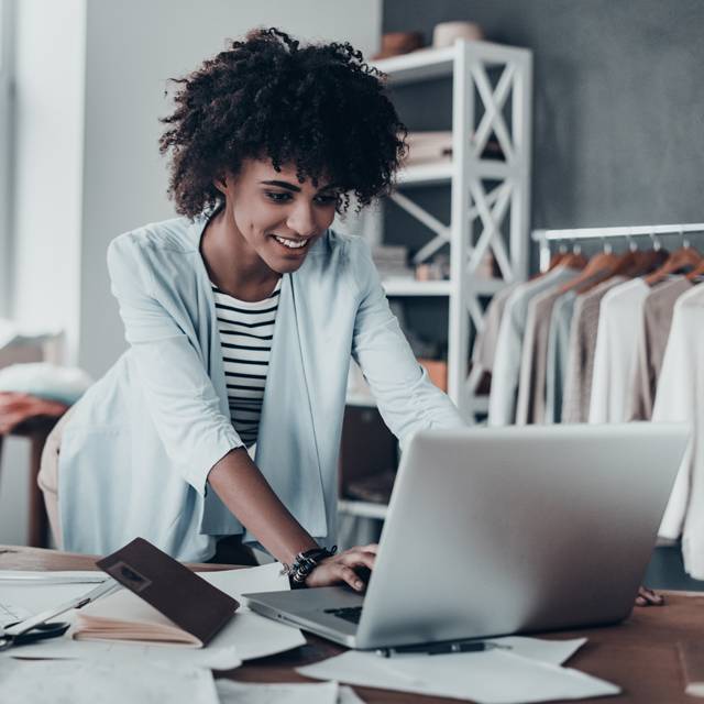Woman looking at laptop screen with clothes rail in background