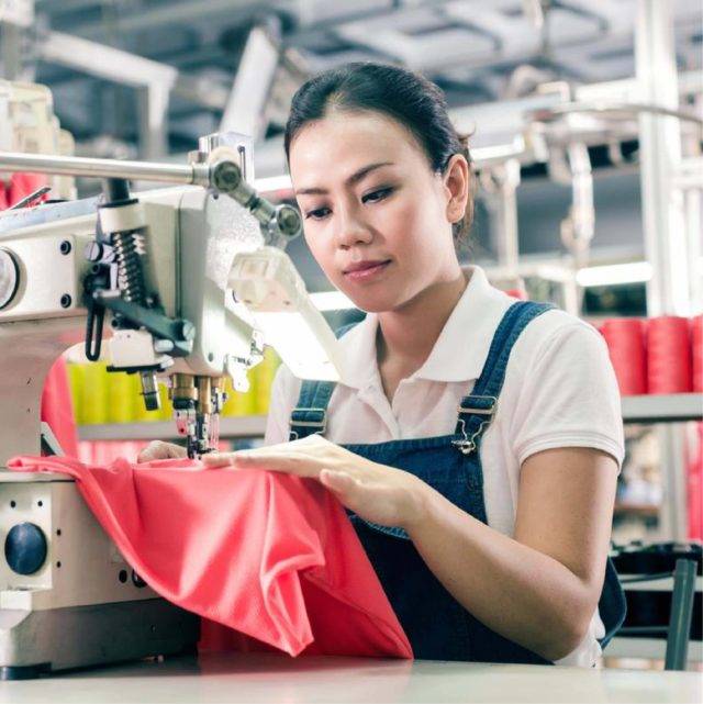 Woman wearing dungarees sewing pink fabric on sewing machine