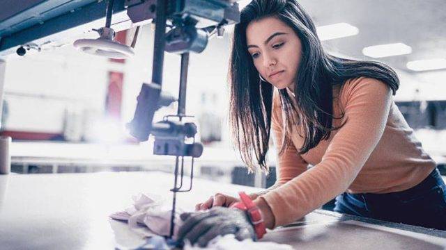 A lady wearing protective glove operating a fabric cutting machine