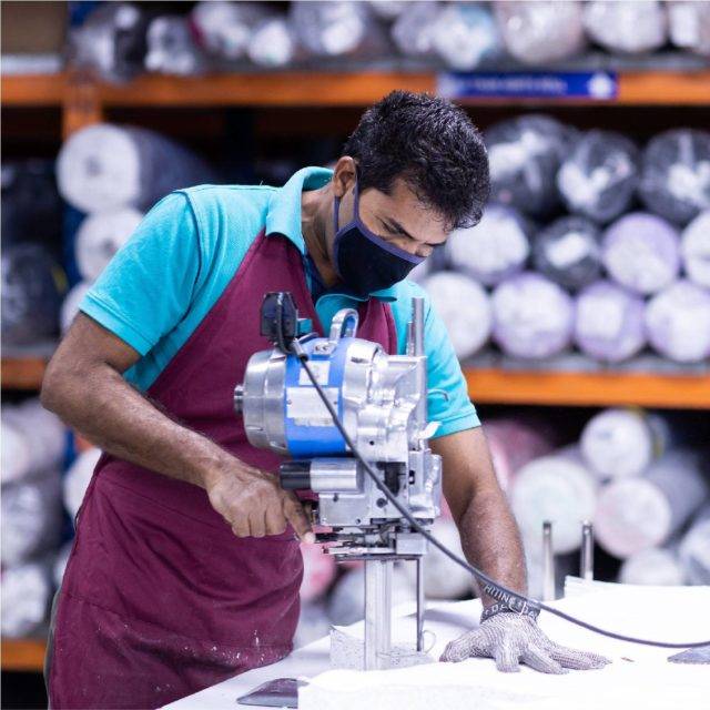 Man wearing protective glove cutting fabric with fabric rolls in the background