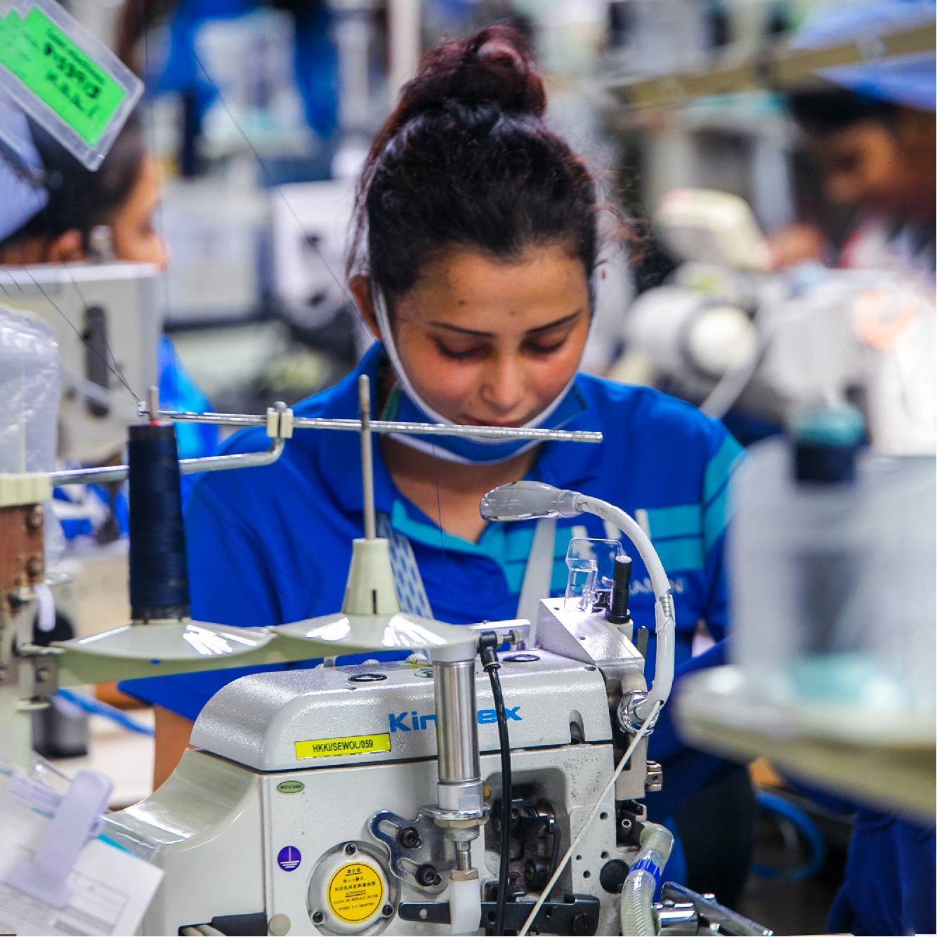 Female seamstress wearing face mask at sewing machine in garment factory