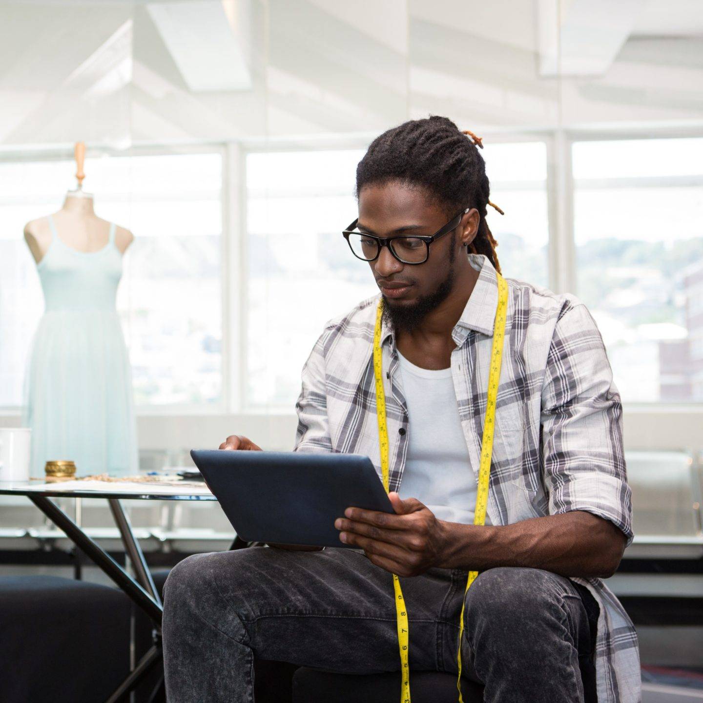 Man with dreadlocks looking at a tablet with yellow measuring tape around neck