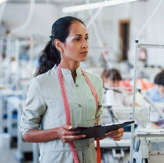 Female supervisor observing sewing line with tablet in garment factory