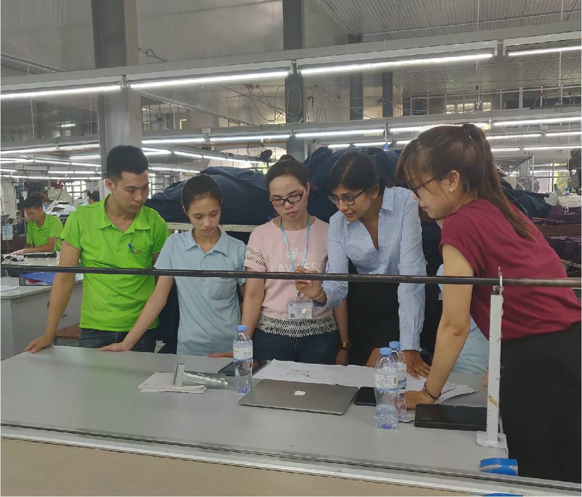 5 Song Hong employees looking at a laptop on cutting table in garment factory