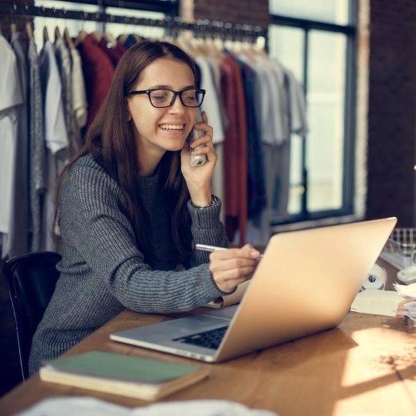 Women on phone pointing at laptop with rail of clothes behind her