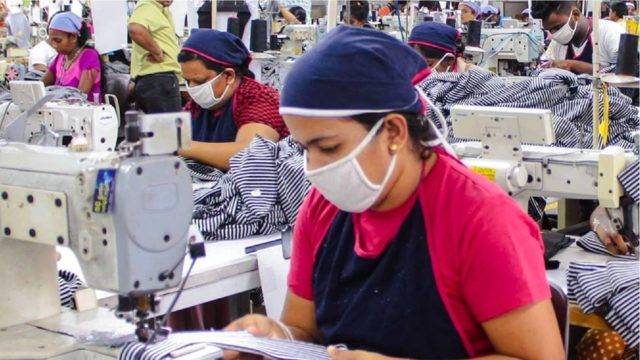 Female seamstress wearing white face mask and blue head scarf in Norwood Fashions garment factory