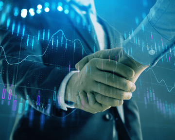 Professionals shaking hands over graphs demonstrating strategic collaboration