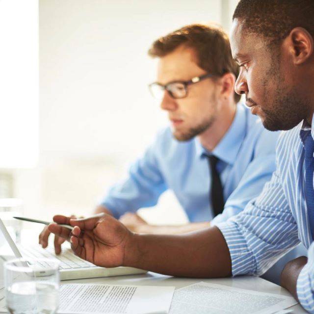 Two business men wearing blue shirts looking at laptop