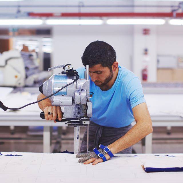 Man wearing protective glove cutting fabric with machine in factory