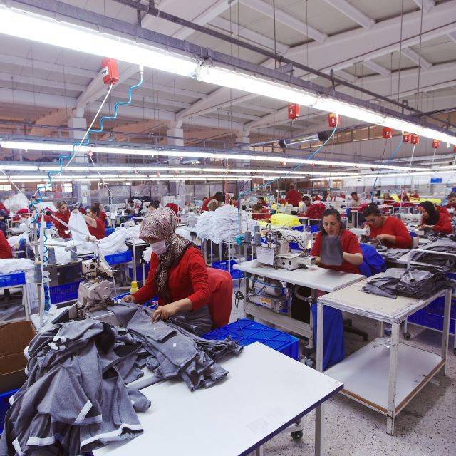 Factory workers wearing red uniform producing blue garments